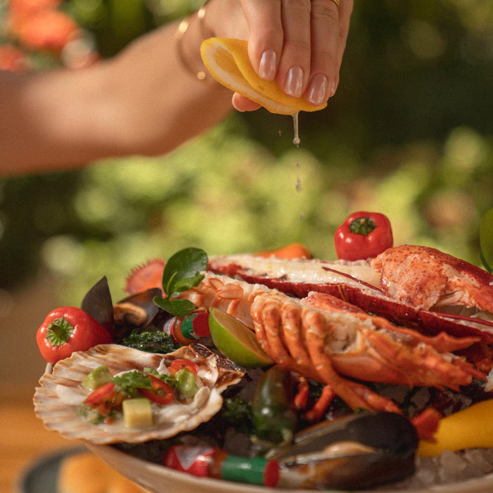 A womans hand squeezing a lemon over a seafood dish.