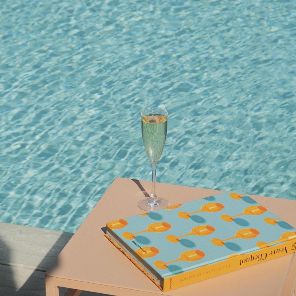 A glass of wine and a book, on a table next to the pool.